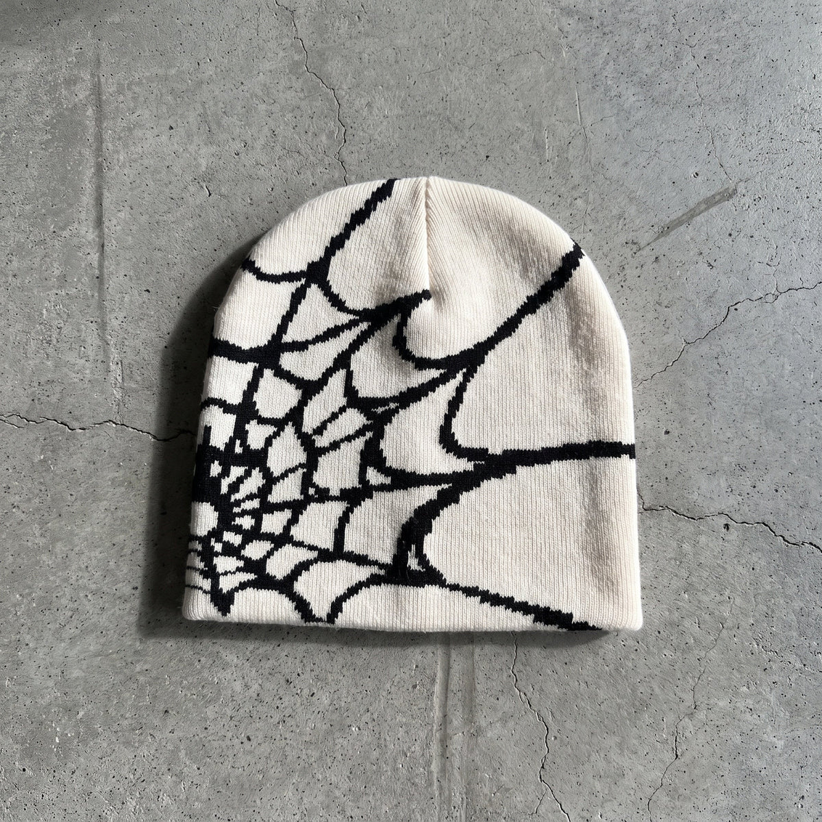 Bone white spider web knit beanie with black web on raw concrete